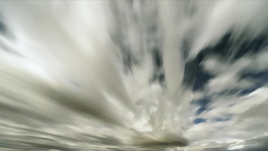 Cumulus clouds quickly move across a bright blue sky and it turns into a star filled night sky