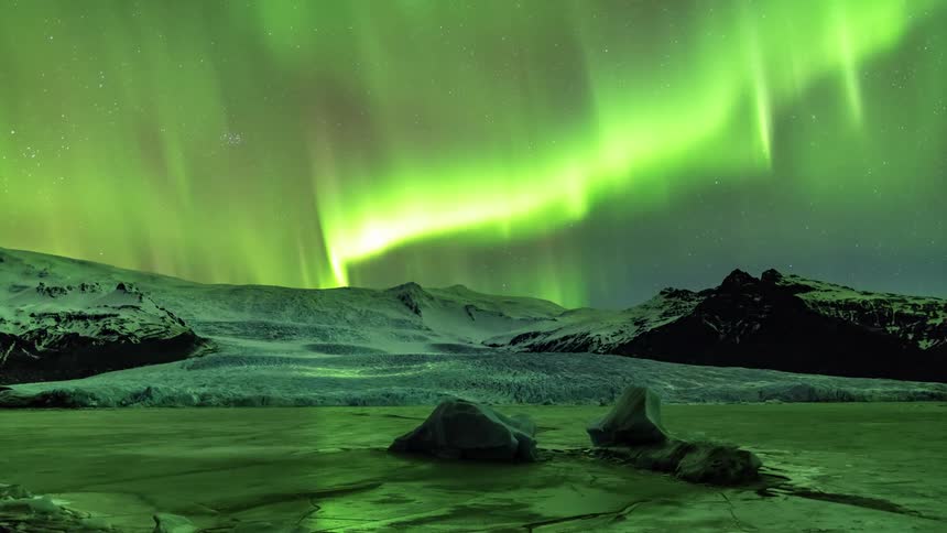 The northern lights are on full display over snowy mountains