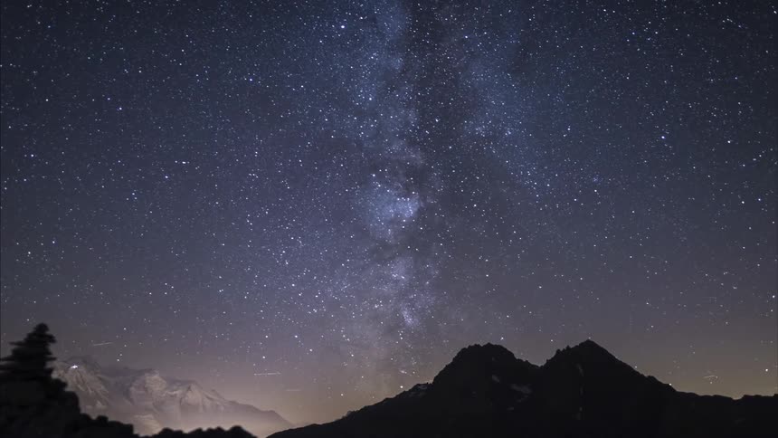 The stars in the night sky glow as the milky way moves over the mountains as daylight arrives