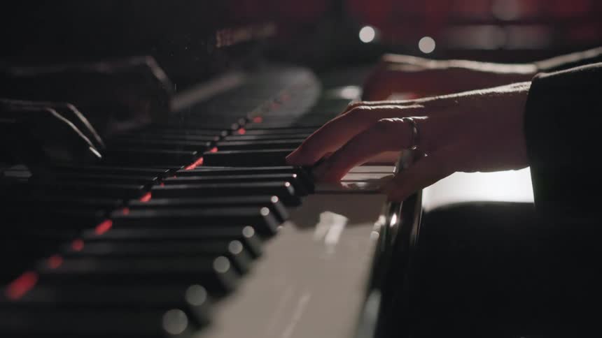 Musician sits at piano in empty theater and plays under bright glaring stage lights