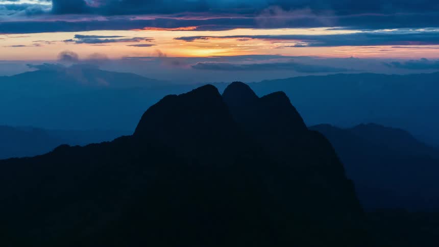 Time lapse of sun shining behind passing clouds over a mountain peak