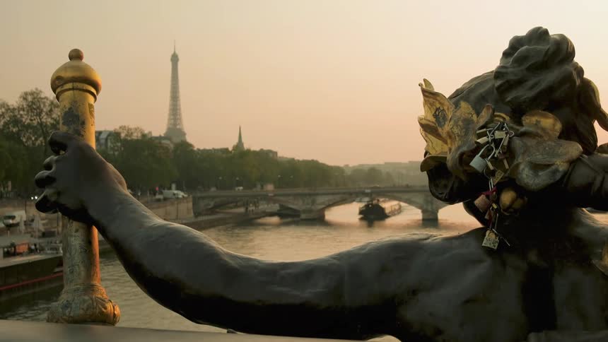 Statue with series of attached locks overlooks river bridge with eiffel tower in the distance