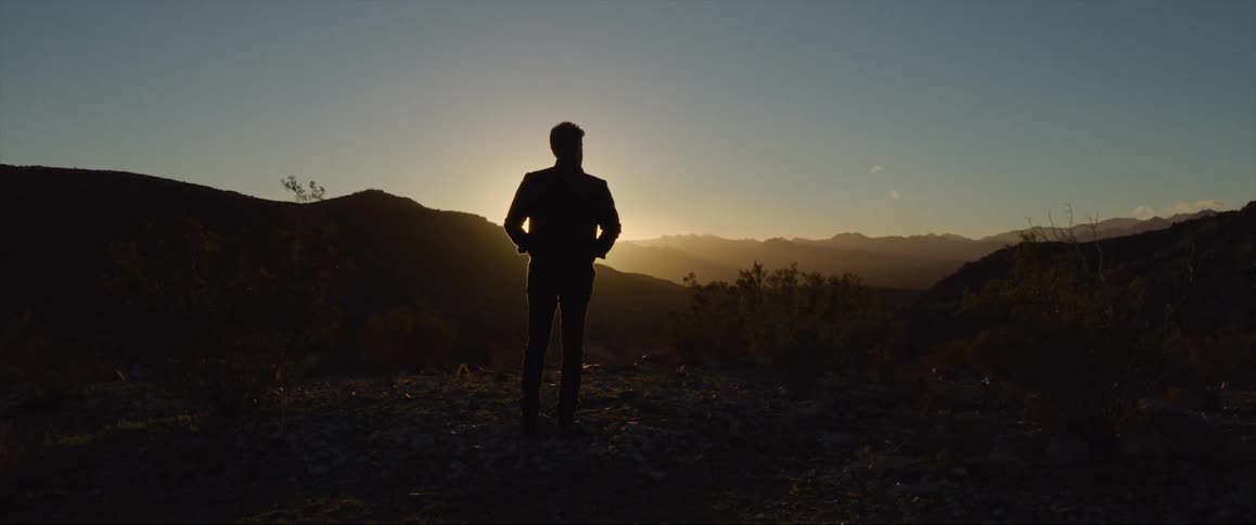 The silhouette of a man is illuminated by the sun which is peeking just above the nearby mountains