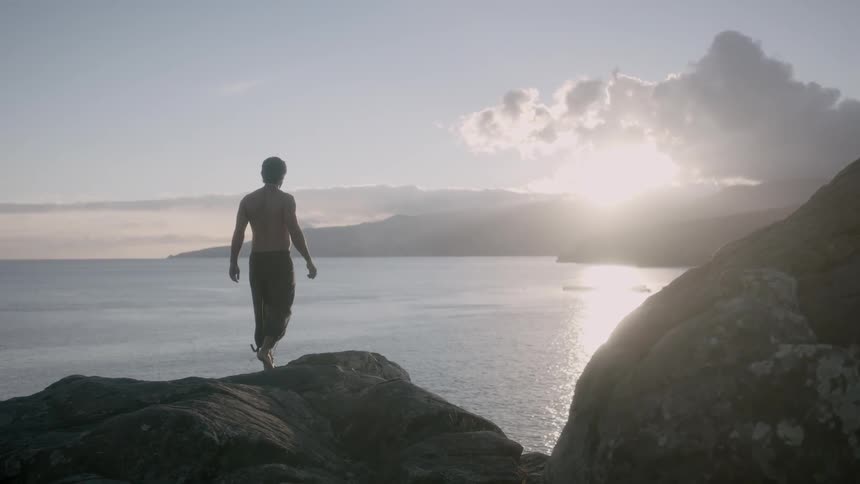 A man walks on a cliff toward the ocean