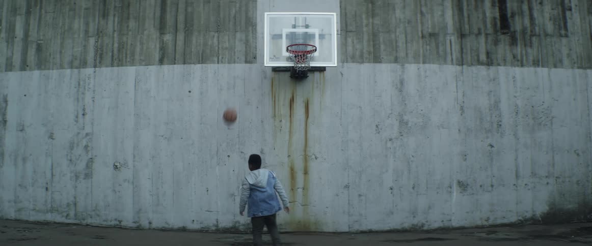 A little boy runs with a basketball and throws it towards the hoop and he turns around after missing the basket