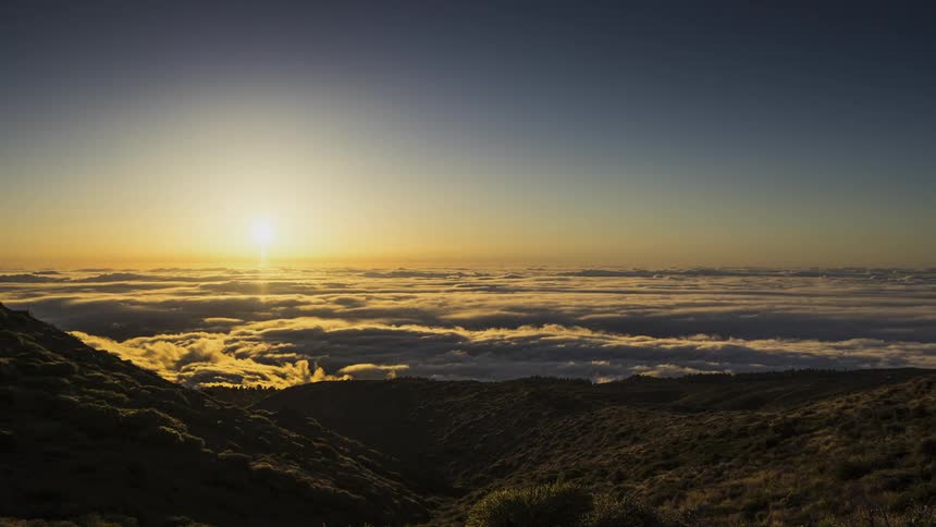 Time lapse of the sun setting over a moving layer of clouds in the mountains