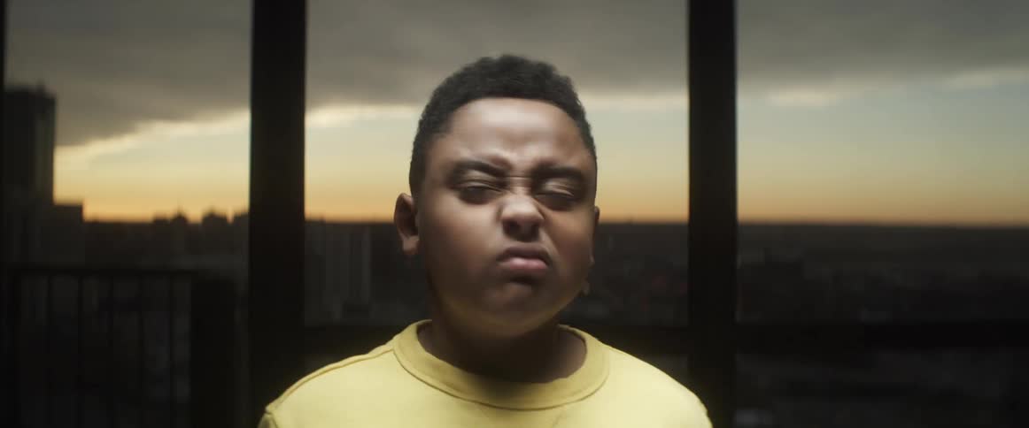 Child stands in front of a window at sunset shaking his head no while his eyes are clenched shut