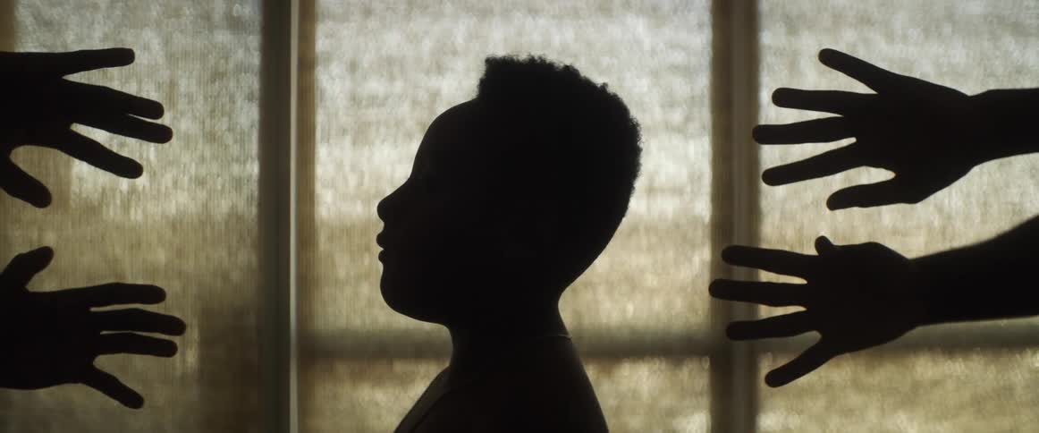 Silhouette of hands reaching for the head of a woman in front of an obscured window
