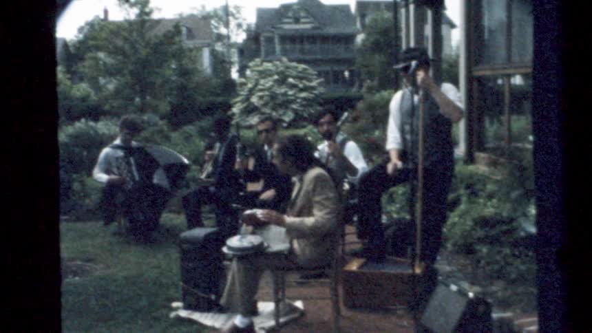 Old time band performing on a small stage in the backyard caught on vintage film