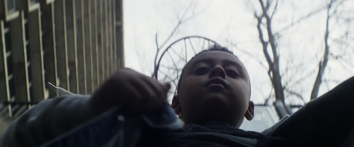 A young boy looks down at the camera as he tightly closes his jacket around himself
