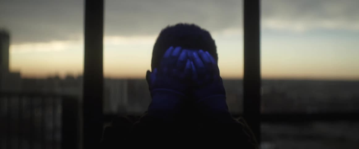 A man covers his face with his hands as colorful lights flash over him
