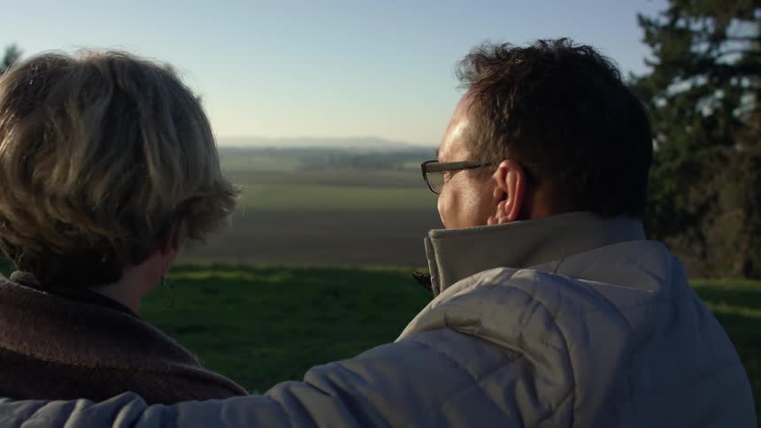 Mature couple sitting together kiss while looking a the sweeping landscape at evening