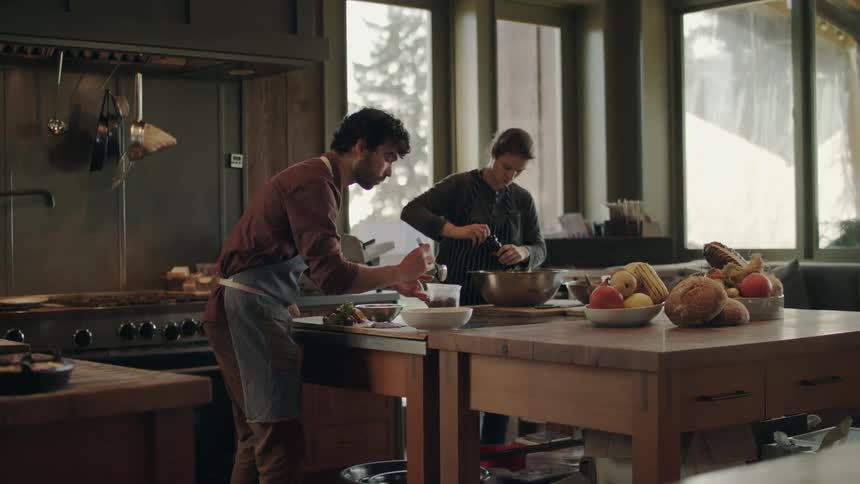 Two people are seen cooking a meal in a kitchen