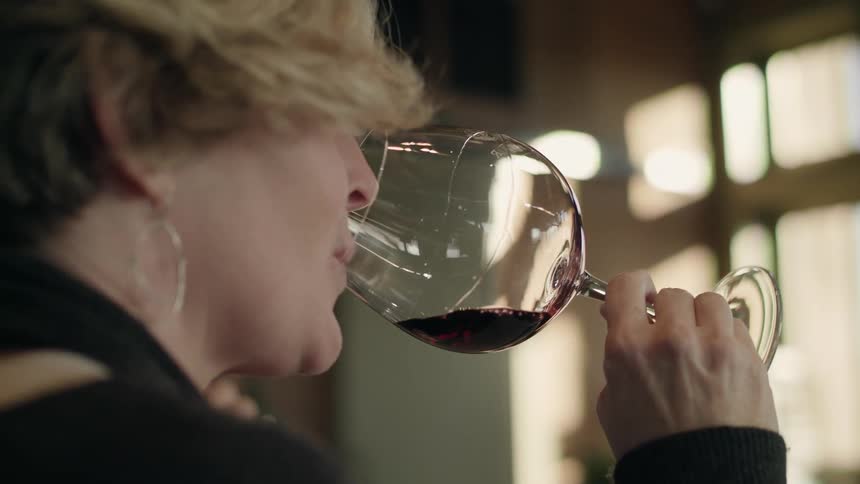 Woman spins wine on a goblet before smelling and drinking it on a wine tasting