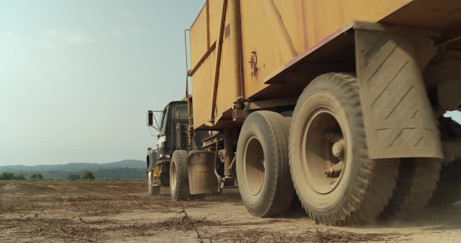 A semi truck is traveling across the dirt and there are mountains in the distance