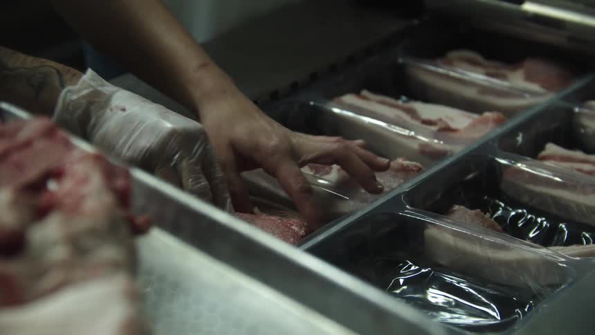 Butcher places cuts of meat on plastic containers in the restaurant kitchen