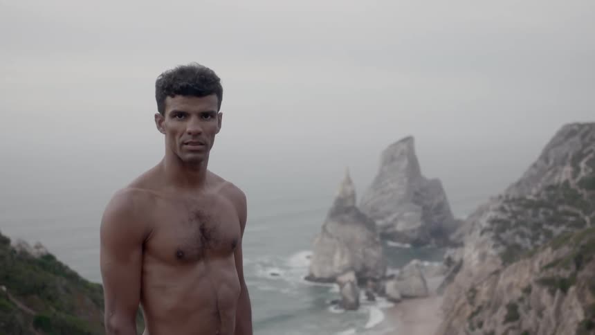 A man is standing up on a hill by the shore
