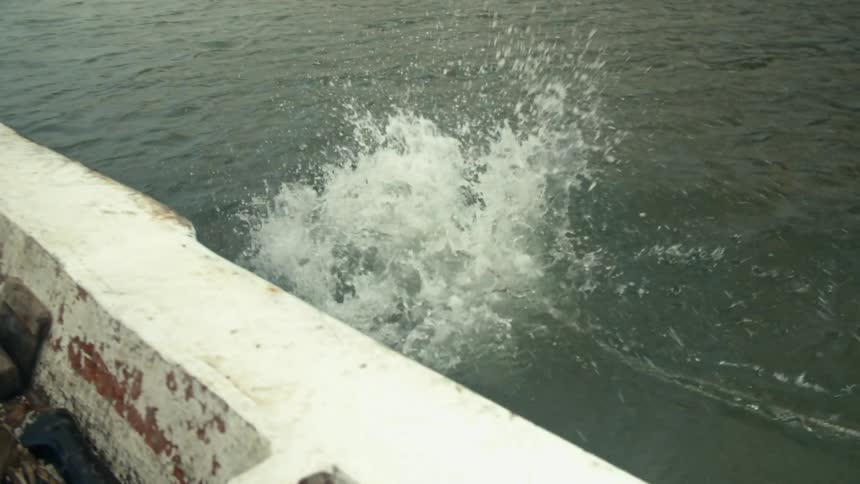 Fishermen throwing cages into a lake from a small moving boat at daytime