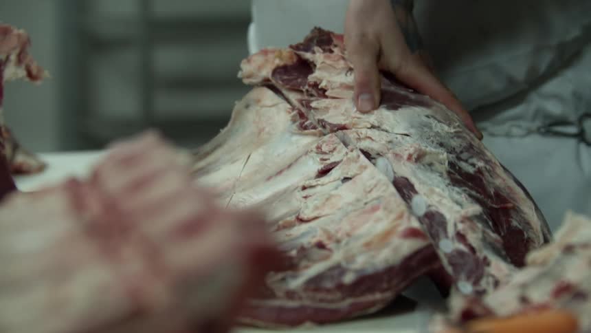 Chef cuts large rib section with knife in kitchen