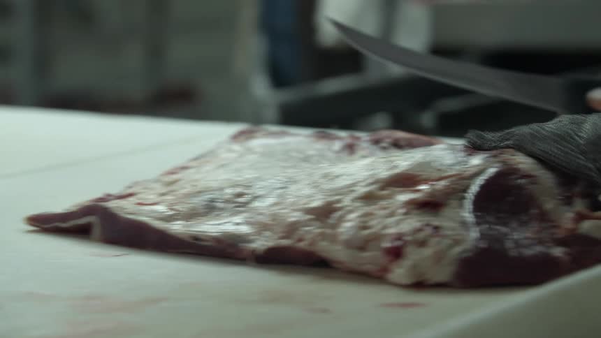A person with a knife skillfully carves a slice of meat on a large cutting board