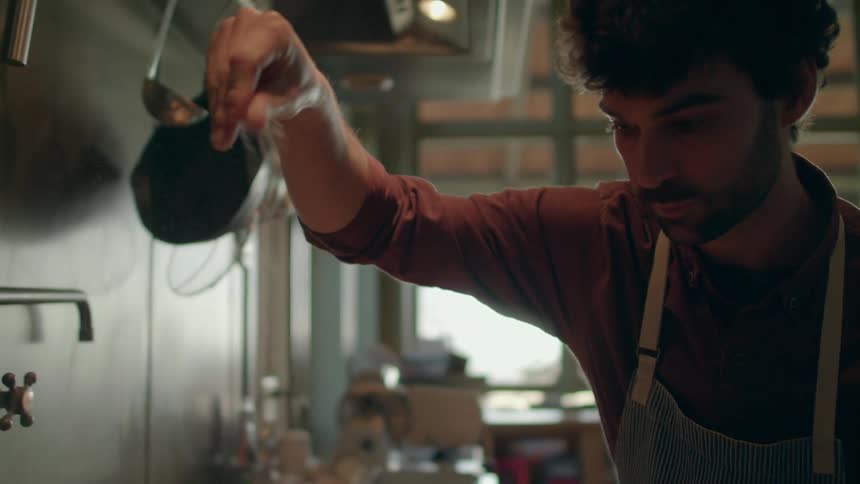 A male cook sprinkles some ingredients atop the food that hes preparing in a kitchen