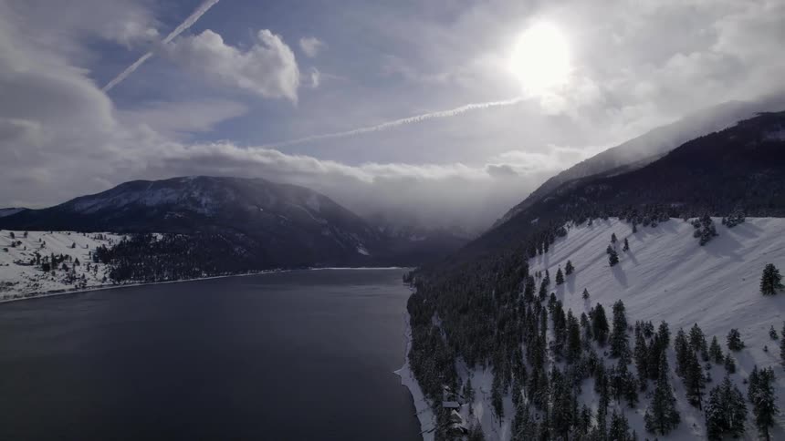 Snow covers the slope of a hill along a river and below a mountain