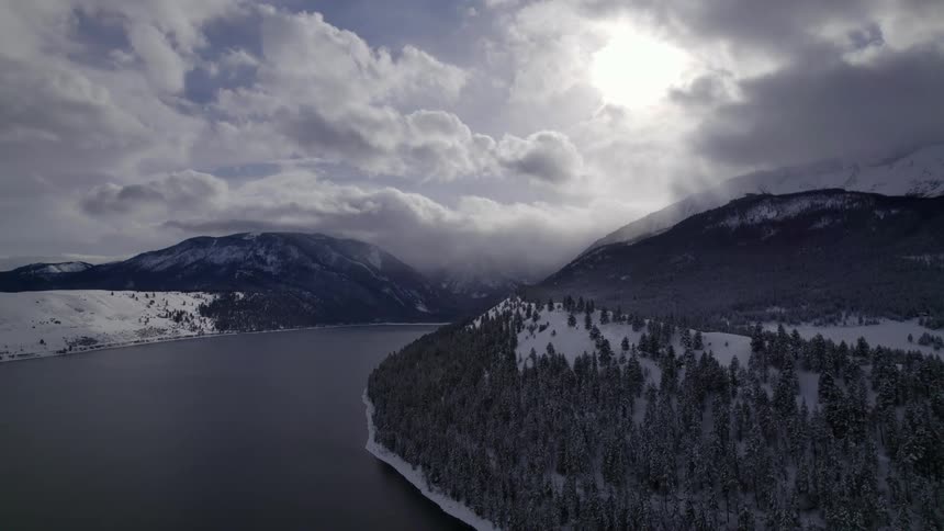A smooth curving lake between snow capped slopes and trees