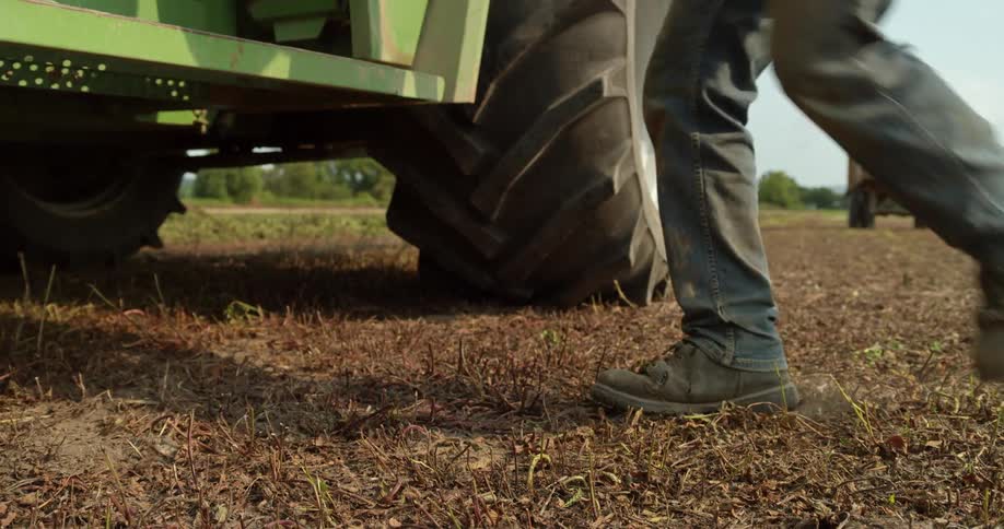 Close up of the legs of a man climbing on a combine harvester on a field in a farm