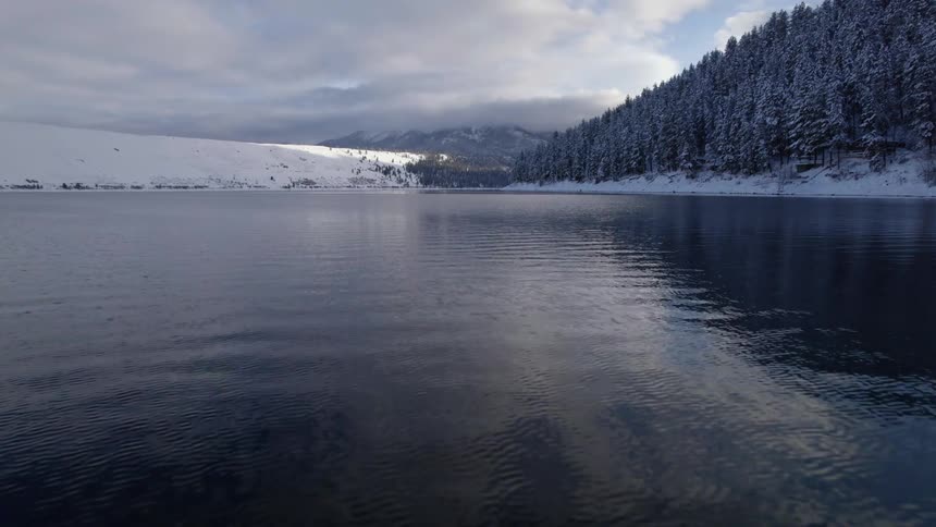 Aerial view of the tranquil surface of a river flowing through the snowy plains near the mountains