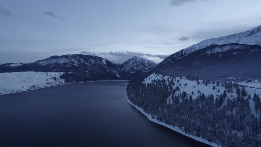 Aerial view of the tranquil surface of a river flowing between snow covered mountains at morning