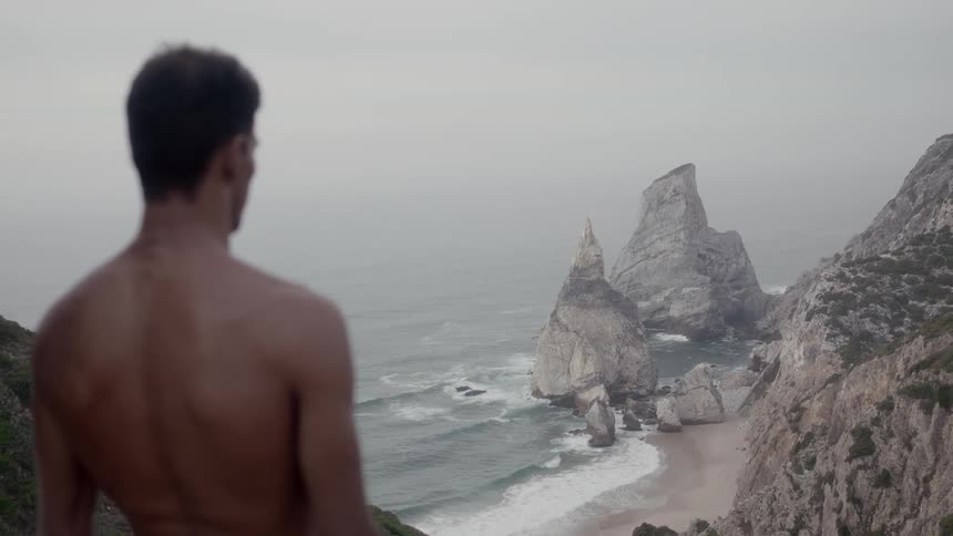 A shirtless man looks down at the beach