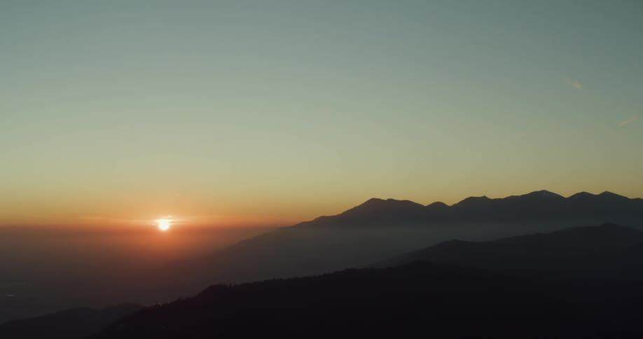 Red sun sets on the horizon over the thin clouds covering the mountains