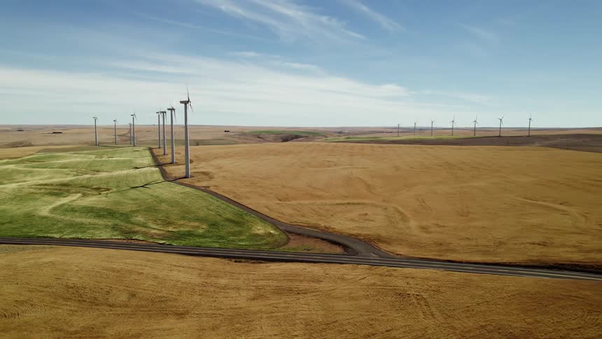 The sun shines upon a turbines spinning on a wind farm