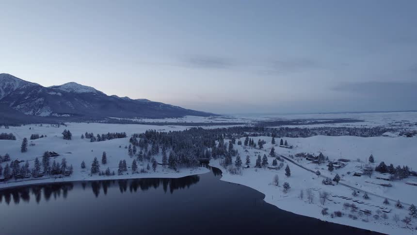 Aerial view of the tranquil surface of a river flowing through the snowy plains near the mountains