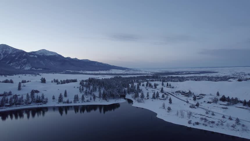Aerial view of the tranquil surface of a river flowing through the snowy plains near the mountains