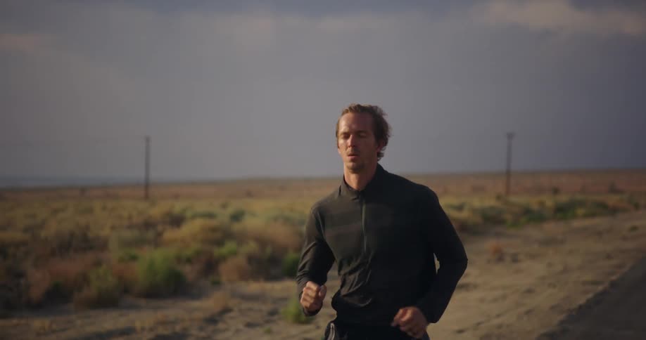 Slow motion footage of a man wearing black clothes jogging on a road through the desert