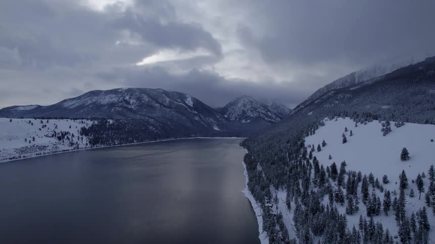 Aerial view of the tranquil surface of a river flowing between snow covered mountains at morning