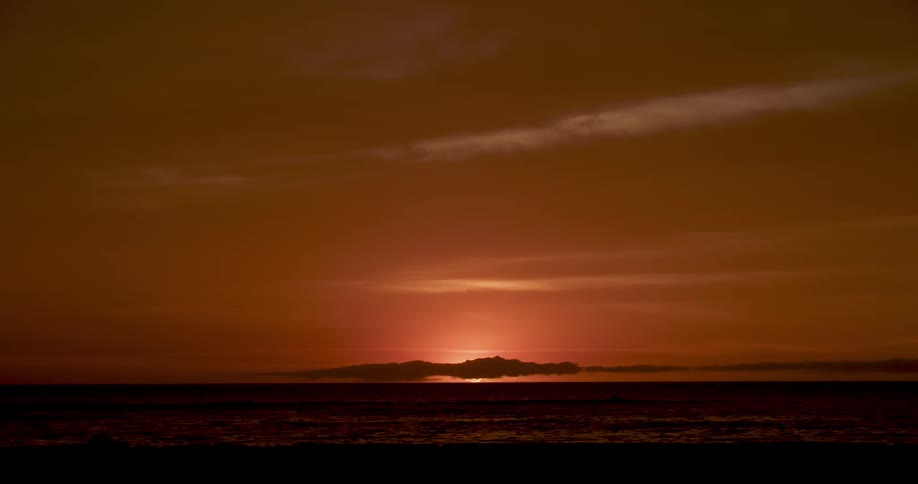 Red sky sunset afterglow behind the silhouette of clouds in the horizon