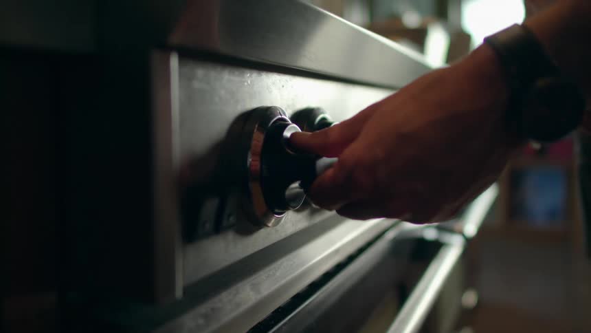 A person reaches out to turn the knob on a large cooking range