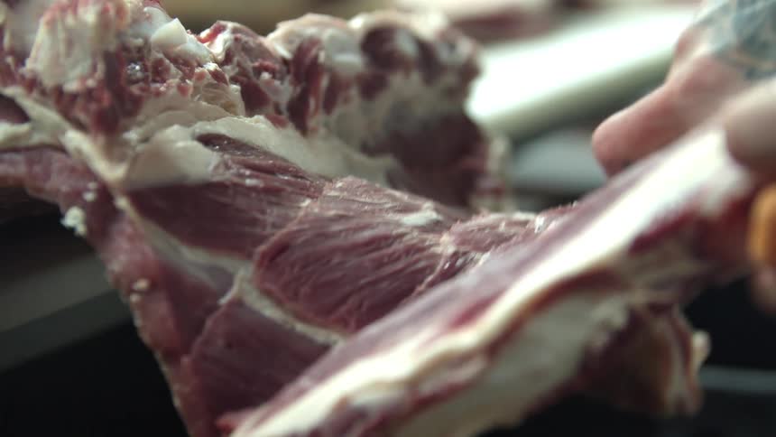 Close up of a butcher cutting a large piece of meat with a sharp knife in the slaughterhouse