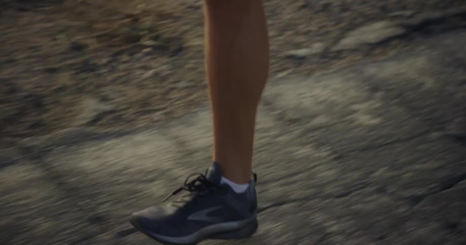 Close up of the legs of a man jogging on the cracked asphalt of a road through the countryside