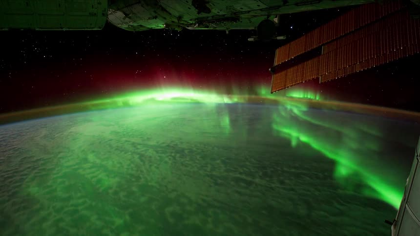 Space station moves over ocean and land passing the aurora borealis