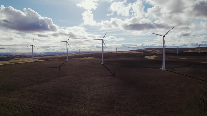 Wind turbines cast long shadows while rotating under a cloudy sky