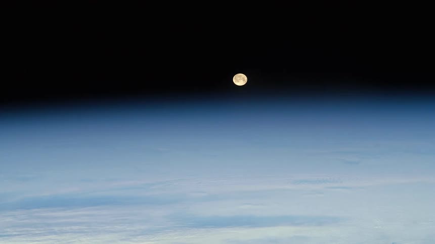 The moon travels over the earth in space as a satellite flies in the darkness