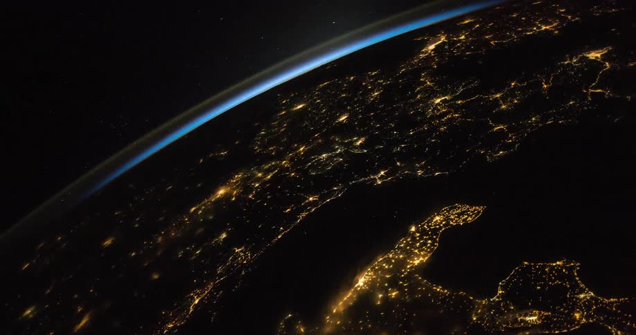 The earth rotates in the darkness and lights glow on the surface as a satellite flies in space