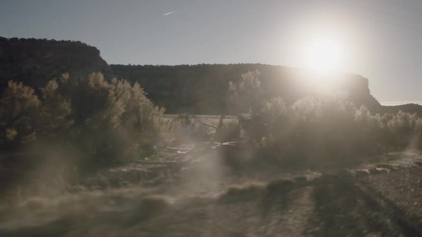 Dust is getting kicked up off a road lined with sagebrush