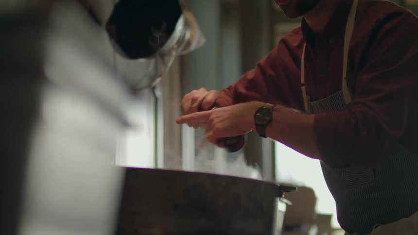 A man is putting spices into a pot using a kitchen apparatus