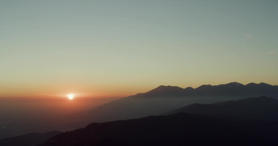 Silhouettes of mountains as the sun sets in a hazy sky in the distance