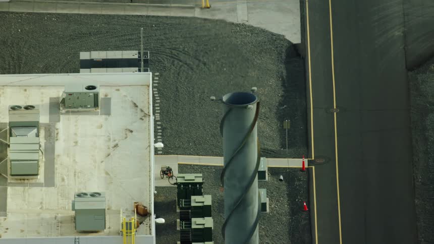 Aerial shot tilting down on a high emissions factory smoke stack producing carbon fiber components
