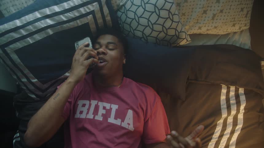 Man in red t shirt lies on bed and talks on smartphone in his room